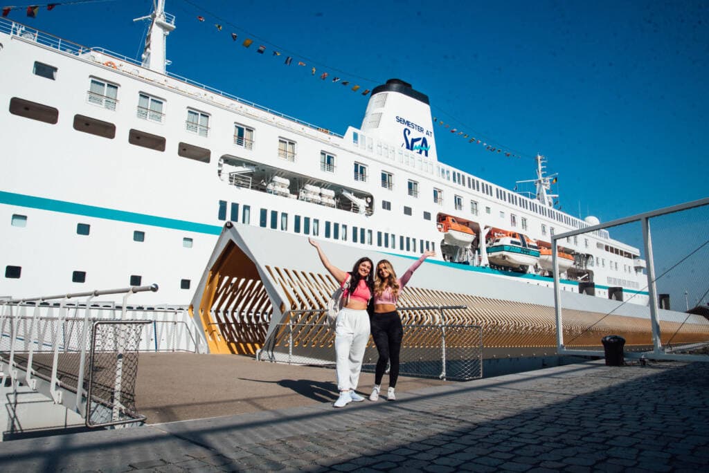 two female students pose in front of a cruise ship